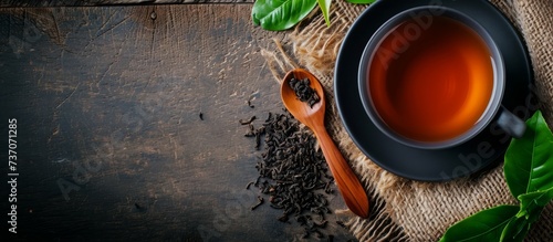 A wooden table set with a cup of tea, tea leaves, and a wooden spoon. The circle of the cup contrasts with the natural elements of wood and plant life photo