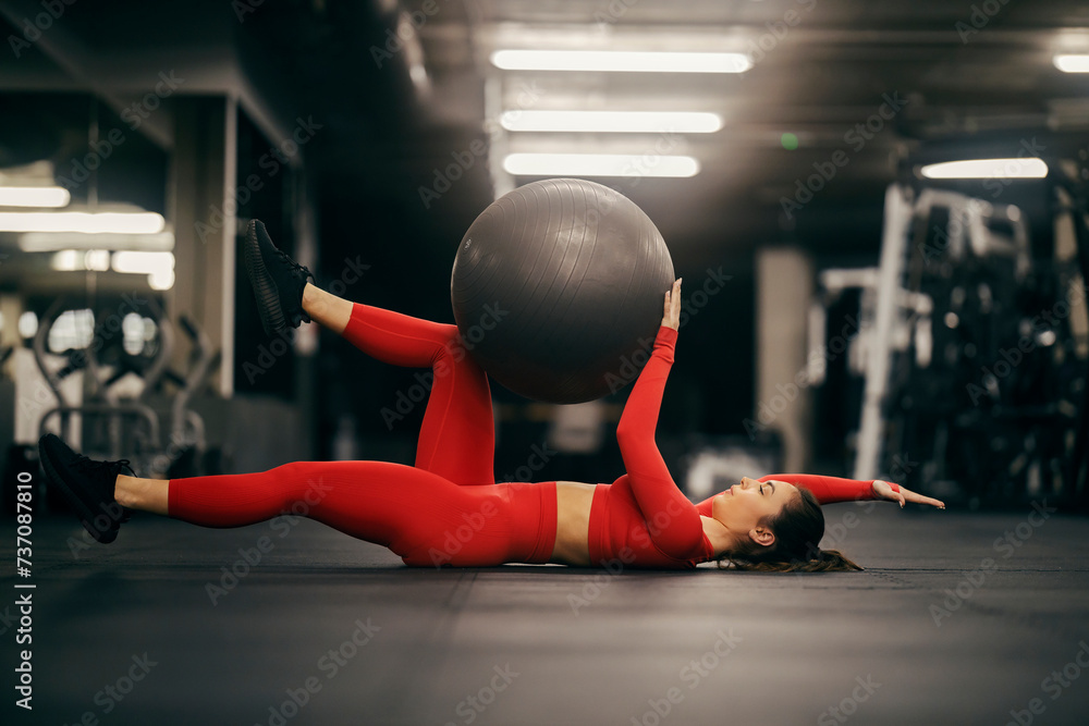 Obraz premium A sportswoman in shape is practicing abs and gluts with fitness ball at gym.