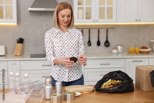 Konstfotografi Smiling woman separating garbage at table in kitchen