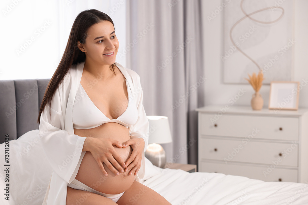 Beautiful pregnant woman in stylish comfortable underwear and robe on bed at home, space for text Beautiful pregnant woman in stylish comfortable underwear and robe on bed at home, space for text