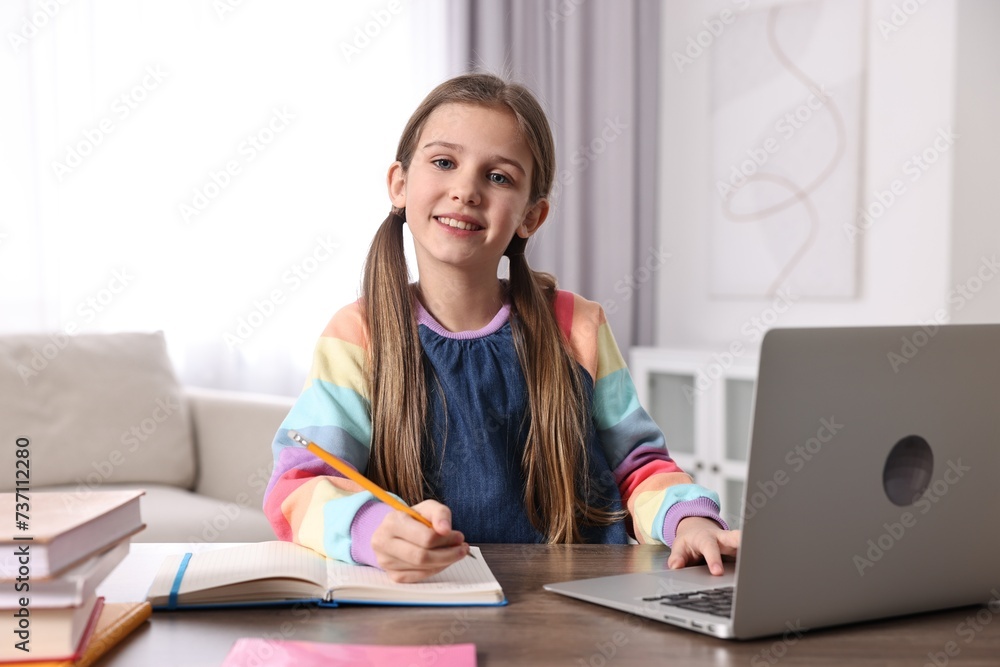 E-learning. Cute girl taking notes during online lesson at table indoors E-learning. Cute girl taking notes during online lesson at table indoors
