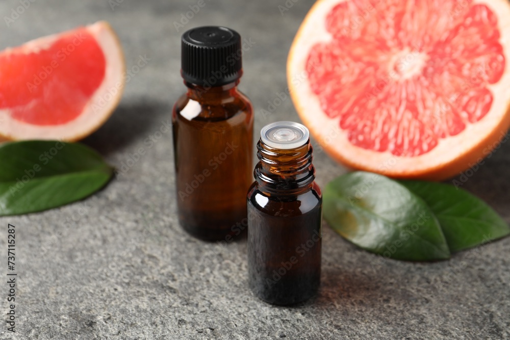 Grapefruit essential oil in bottles, leaves and fruit on dark textured table, closeup Grapefruit essential oil in bottles, leaves and fruit on dark textured table, closeup