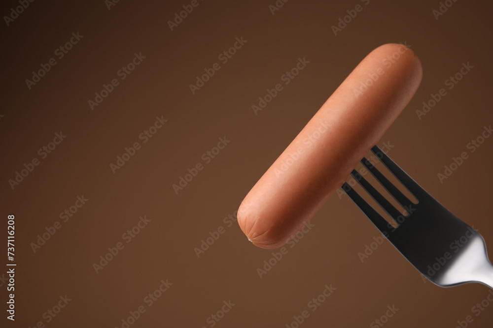 Delicious boiled sausage on fork against brown background, closeup. Space for text Delicious boiled sausage on fork against brown background, closeup. Space for text