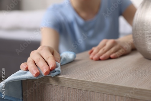 Woman with microfiber cloth cleaning wooden chest of drawers in room, closeup photo