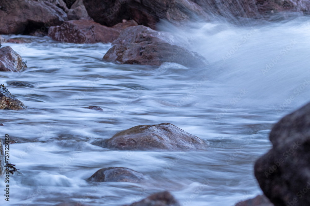 Naklejka premium Waves breaking over rocks on the sea shore with the waves smoothed by long exposure