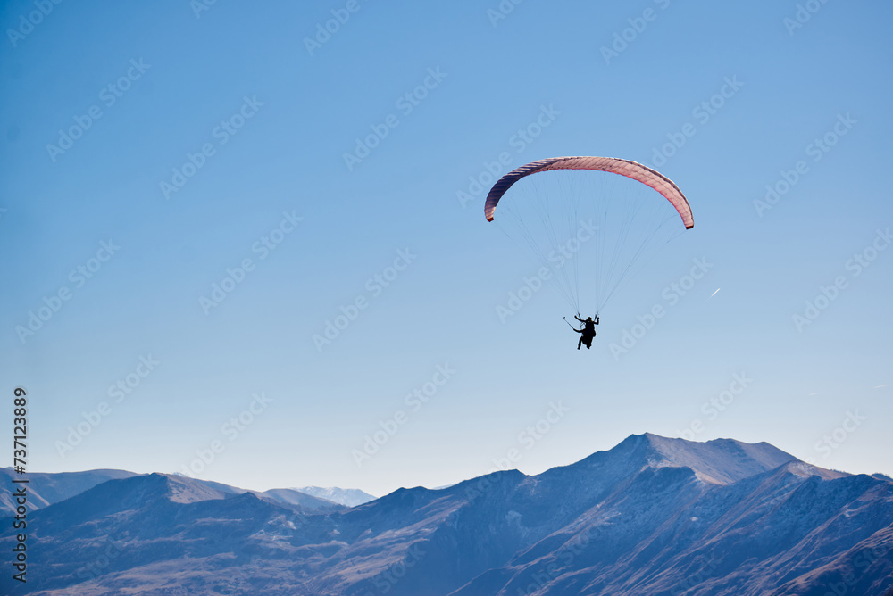 Floating effortlessly above the earth, the paraglider enjoys panoramic views of the brown mountain tops. Floating effortlessly above the earth, the paraglider enjoys panoramic views of the brown mountain tops.