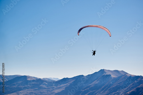Floating effortlessly above the earth, the paraglider enjoys panoramic views of the brown mountain tops.