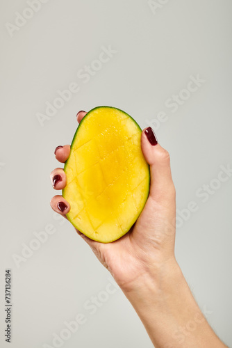 object photo of gourmet juicy mango in hand of young unknown female model on gray backdrop