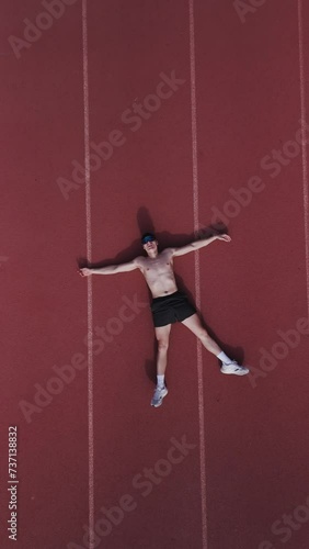 Runner on athletics track seen from above in zenithal view. He throws himself to the ground exhausted from the race. Vertical drone video. Concept of giving the maximum of yourself