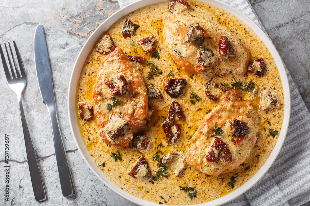 Marry Me Chicken, chicken breasts sauteed in cream sauce with sundried tomatoes, thyme, red pepper flakes closeup on the plate on the table. Horizontal top view from above
