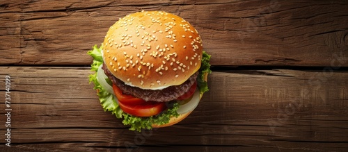 A hamburger, a staple food in fast food cuisine, composed of a bun and various ingredients, is placed on a wooden table