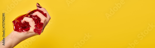 Φωτογραφία unknown female model squeezing red tasty jello in her hand on vibrant yellow bac