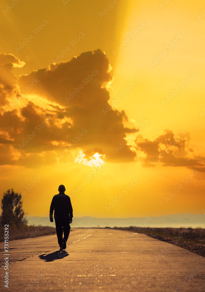 A young man walks along a concrete road and looks at a beautiful golden sunset. Vertical image