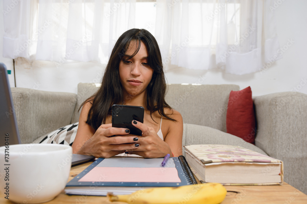 young latin woman at home working and sending messages on phone young latin woman at home working and sending messages on phone