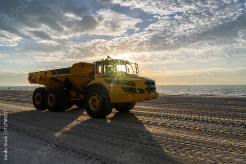 Articulated hauler mining type dump truck, in motion, carrying sand for a restoration project on a beach as the sun rising over the gulf of Mexico, Sanibel Island, Florida