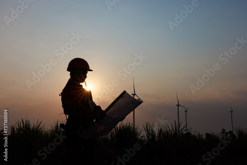 Silhouette of young female engineer holding a blueprint standing beside agricultural sugarcane and wind turbine morning sun star light effect background,..