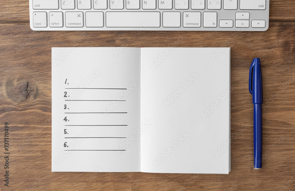 Spread notebook with written lists, keyboard and blue pen on brown wooden desk Spread notebook with written lists, keyboard and blue pen on brown wooden desk