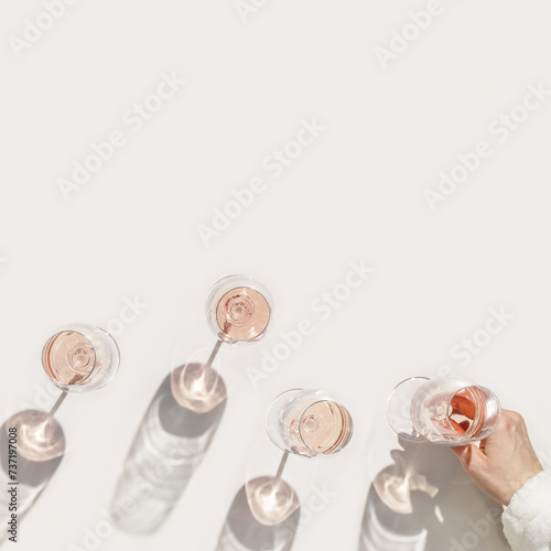 Set glasses of rose wine at wine party, Minimal concept. Top view crystal wineglass in female hand at sunlight, sun shadow and glare, beige pink colored, alcohol drink background, copyspace