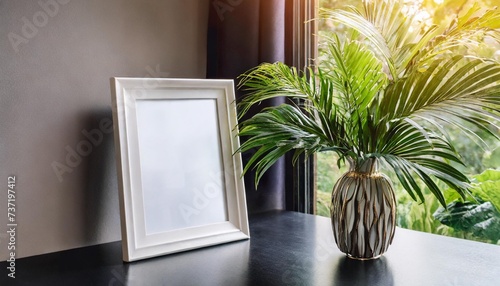 blank white picture frame mockup next to a window modern table white plexiglass top black legs still life composition with green palms in vase