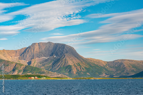Beautiful seascape in North Norway. View of the picturesque coast with the mountains and peaks and traditional red houses from the boat. Travel Scandinavian background