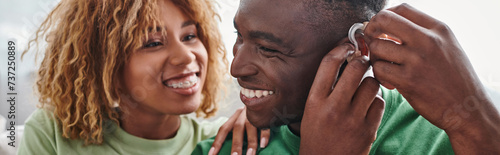 deaf and happy african american man wearing hearing aid near girlfriend, health device banner photo
