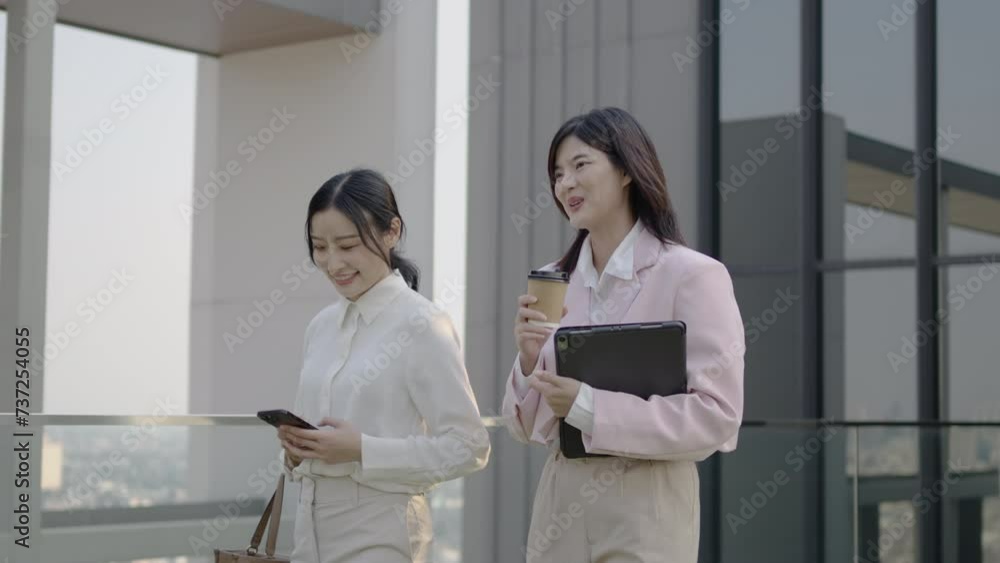 Two business partners woman in formal suits standing outdoors office building terrace in downtown city discuss upcoming project and deals holding digital tablet and coffee cup Two business partners woman in formal suits standing outdoors office building terrace in downtown city discuss upcoming project and deals holding digital tablet and coffee cup