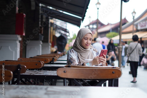 Indonesian Woman wearing Hijab Engaging in Digital Conversations at Cafe Bench