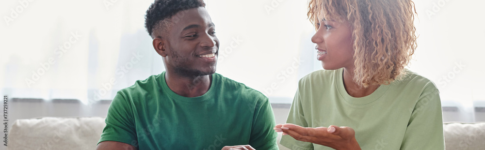Obraz premium happy African American couple communicating with sign language while sitting on couch, banner