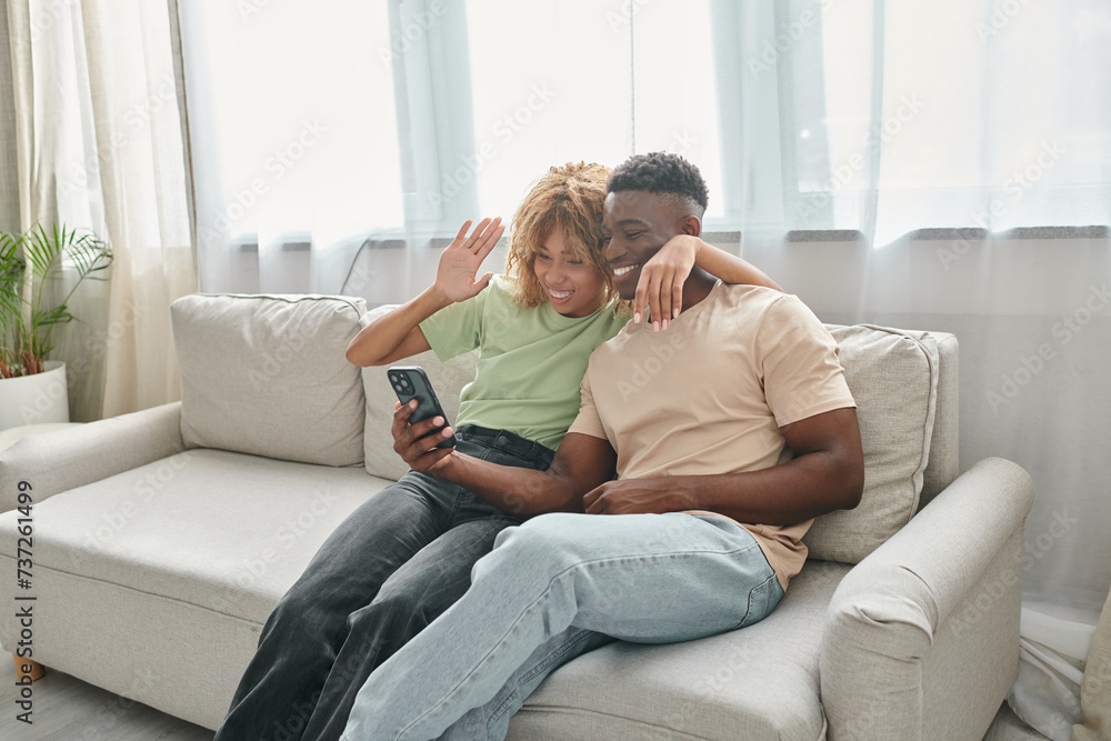happy african american couple video chatting on a smartphone while sitting on couch together