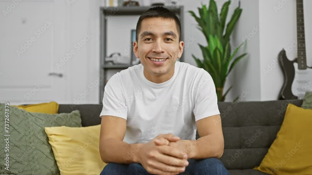 A smiling hispanic man sitting comfortably in a cozy living room with modern decor and a guitar in the background. A smiling hispanic man sitting comfortably in a cozy living room with modern decor and a guitar in the background.