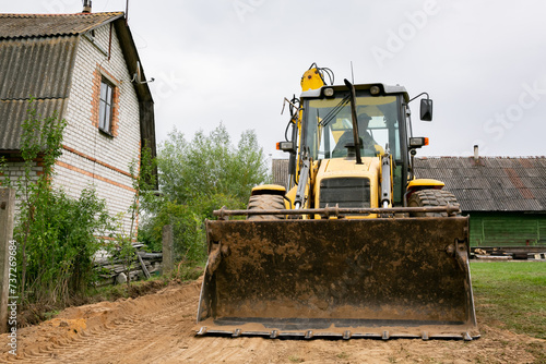 A tractor levelling and clearing the construction site. Bulldozer earth work. Working process at a the back yard. Fence building. Tractor bucket close up. Moving the ground. Copy space. Front view