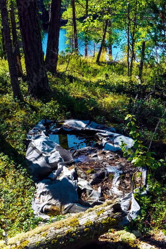 Clogging of the environment with ubiquitous plastic. This single-person rowing plastic boat has rotted on the shore of a forest lake, it crumbles into dust in the sun