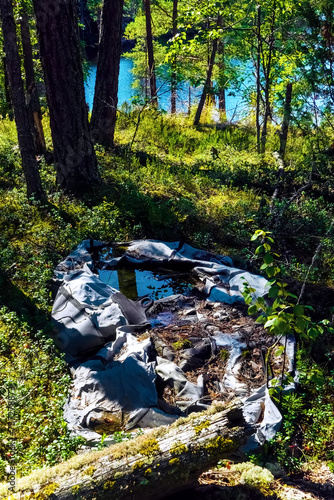 Clogging of the environment with ubiquitous plastic. This single-person rowing plastic boat has rotted on the shore of a forest lake, it crumbles into dust in the sun photo