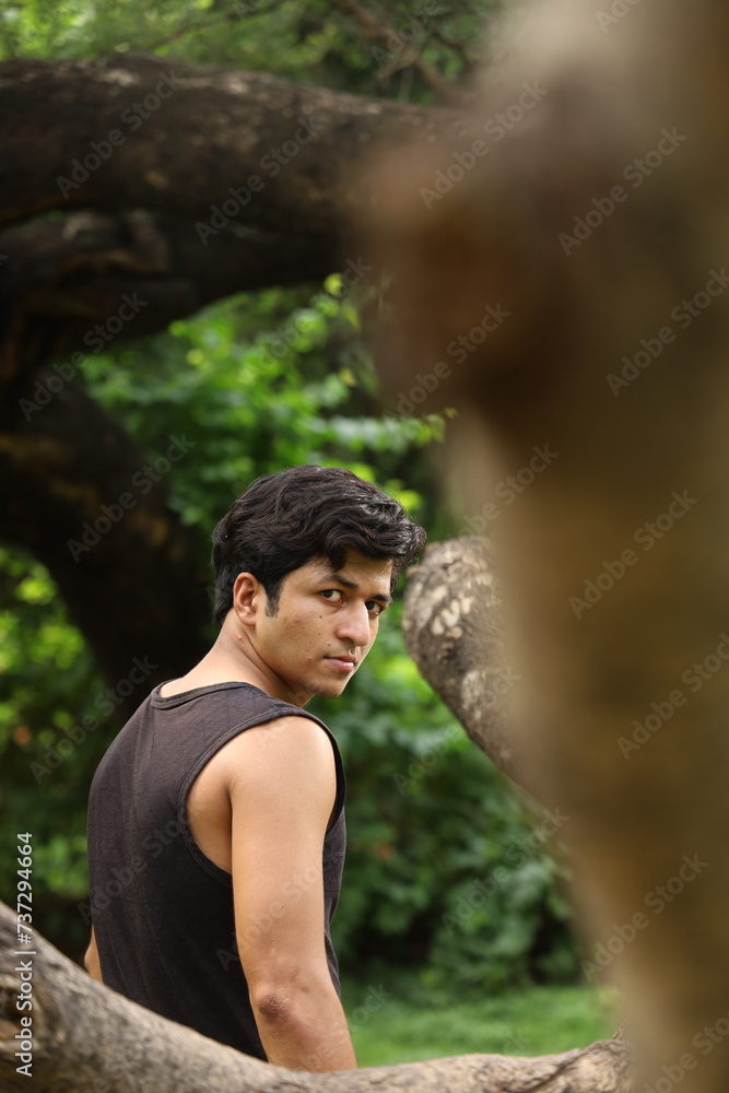 Handsome young Man standing in public city park. Looking at the camera. tree in bokeh Handsome young Man standing in public city park. Looking at the camera. tree in bokeh