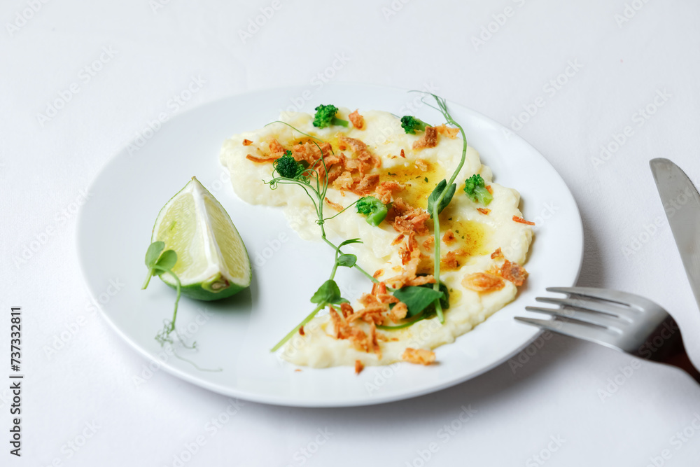 Garnish mashed potatoes with onion, sauce and micro greens, and slice of lime on white plate. Top view.