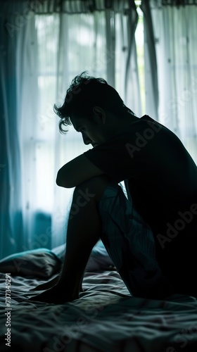 A shadowy silhouette of a lonely depressed man sitting in bed. Sad and melancholy man with crushing weight of his thoughts. Concept of depression or insomnia.