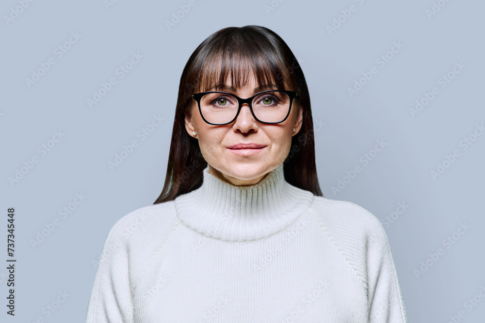 Headshot portrait middle-aged smiling woman in white sweater on gray background