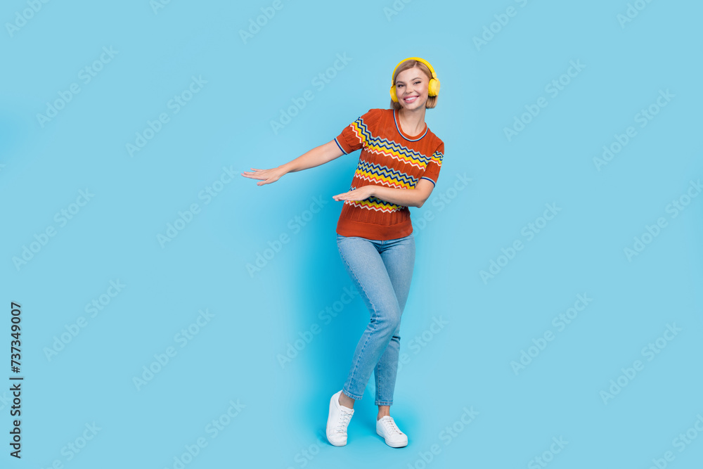 Full length photo of pretty girl wear strited t-shirt jeans in headphones dancing near empty space isolated on blue color background Full length photo of pretty girl wear strited t-shirt jeans in headphones dancing near empty space isolated on blue color background