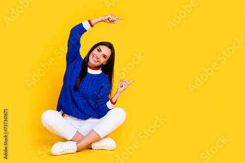 Full body photo of beautiful brunette woman dressed blue knitwear point fingers billboard in your city isolated on yellow color background © deagreez