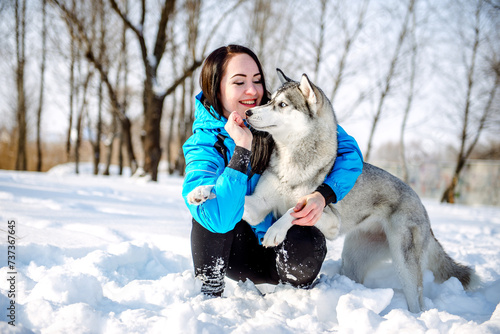 Girl with a cute husky in a winter park. Dog playing in the snowy forest