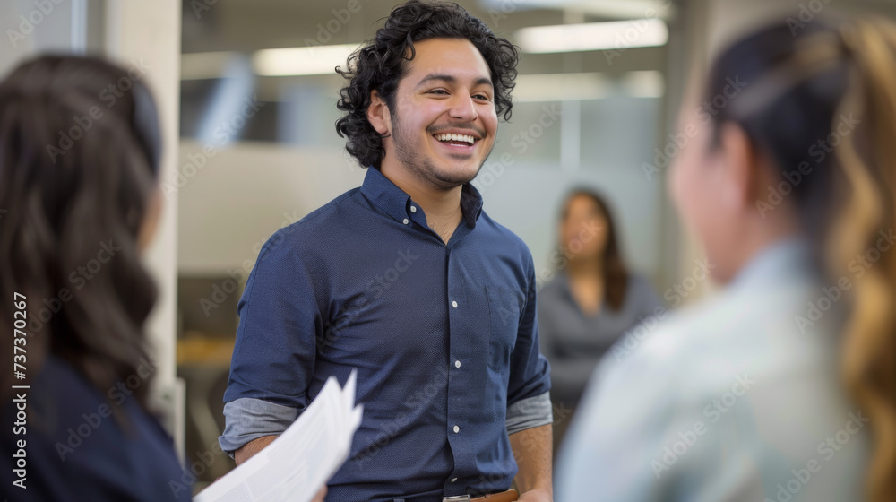 A man in a casual shirt is laughing and holding a document during a cheerful interaction with colleagues in an office setting. - obrazy, fototapety, plakaty 