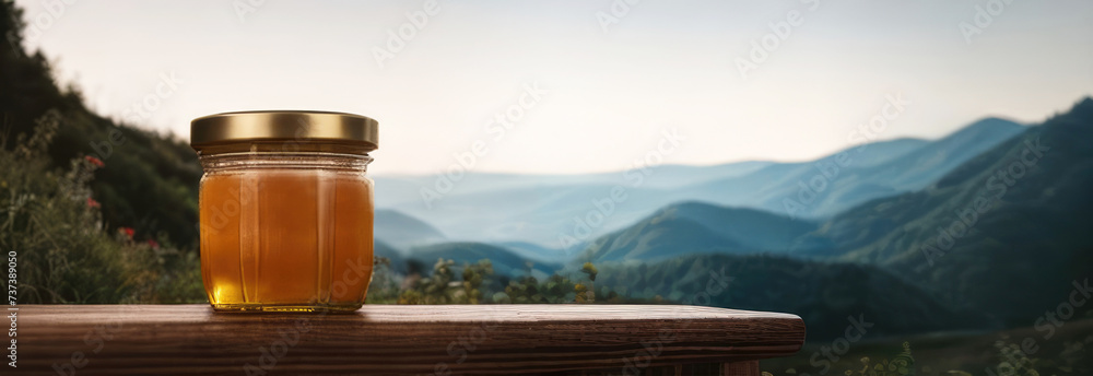 Banner Honey in a glass jar on a wooden surface on the background of a mountain landscape. Beekeeping products. Fresh honey from honeycomb, flower honey, variegated herbs. Place for text - obrazy, fototapety, plakaty 