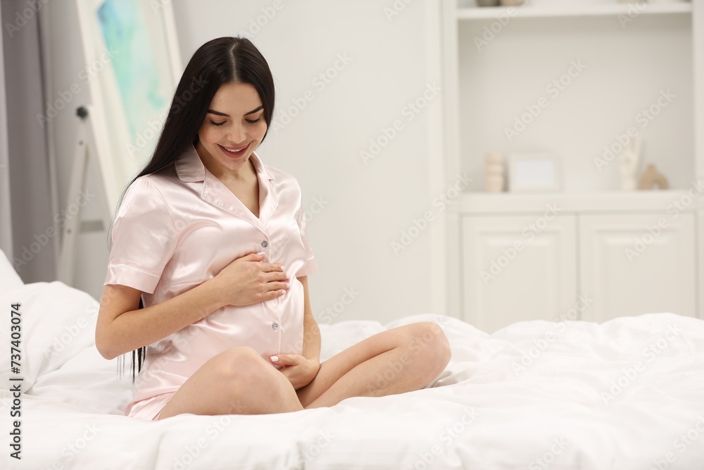 Happy pregnant woman on bed at home, space for text Happy pregnant woman on bed at home, space for text