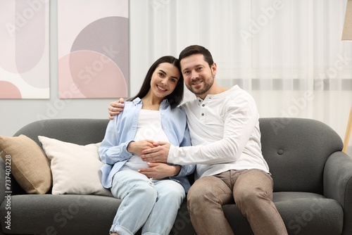 Portrait of happy pregnant woman with her husband on sofa at home