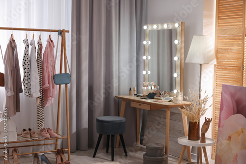 Makeup room. Stylish dressing table with mirror, chair and clothes rack indoors photo