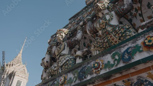 close-up of the ornate architectural details of Wat Arun, with intricate statues and colorful floral-patterned decorations against a clear sky. The temple's characteristic spires are visible in the ba photo