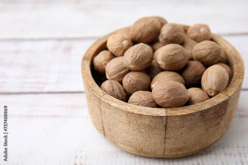 Whole nutmegs in bowl on light wooden table, closeup. Space for text Whole nutmegs in bowl on light wooden table, closeup. Space for text