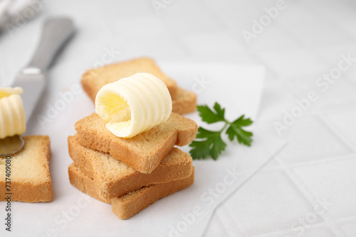 Tasty butter curls, knife and pieces of dry bread on white tiled table, closeup. Space for text