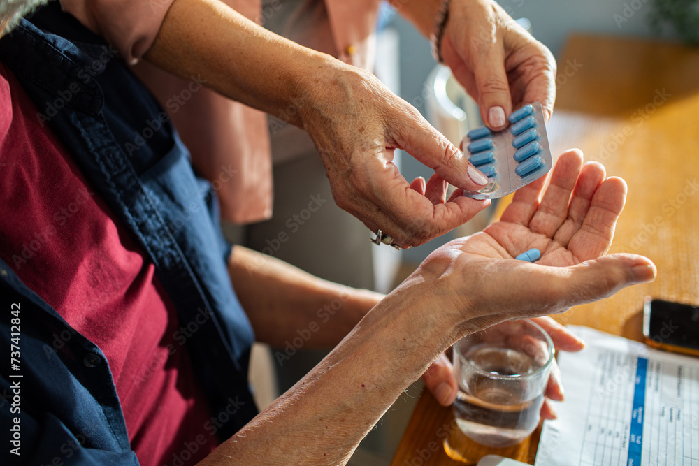 © Marko Geber - Senior hands dispensing medication from a pill organizer into palm with water glass on table © Marko Geber - Senior hands dispensing medication from a pill organizer into palm with water glass on table