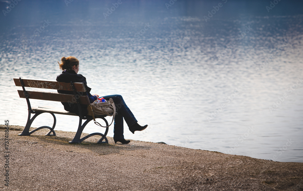 Thoughtful woman sitting alone on a lakeside bench, immersed in quiet contemplation